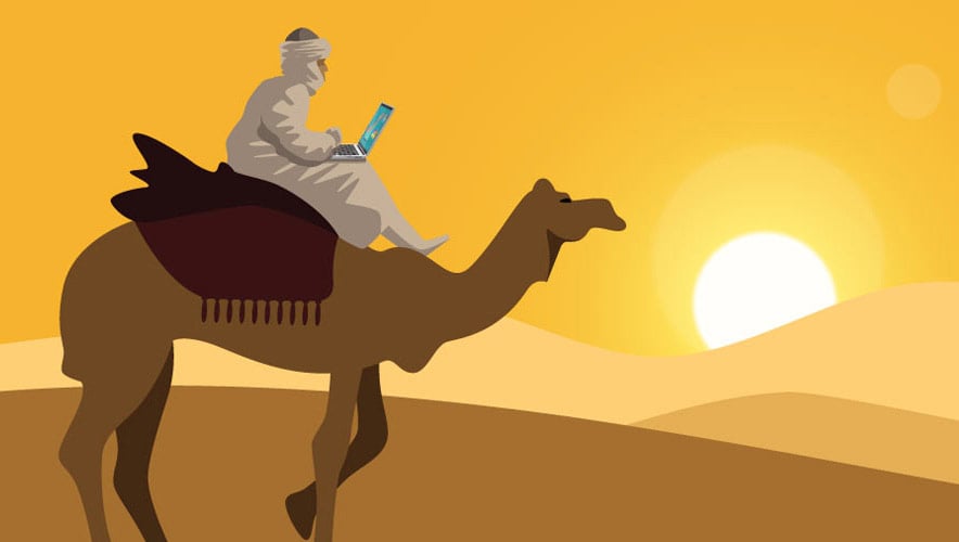 A digital nomad rides a camel across the desert while working remotely. 15.5 million American workers describe themselves as digital nomads.