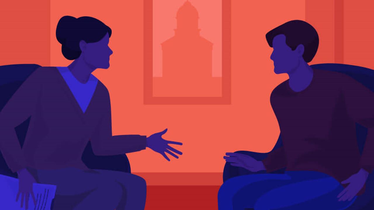 Two people sit in an orange room, talking tensely about a serious matter. A framed school building silhouette is seen outside the window.