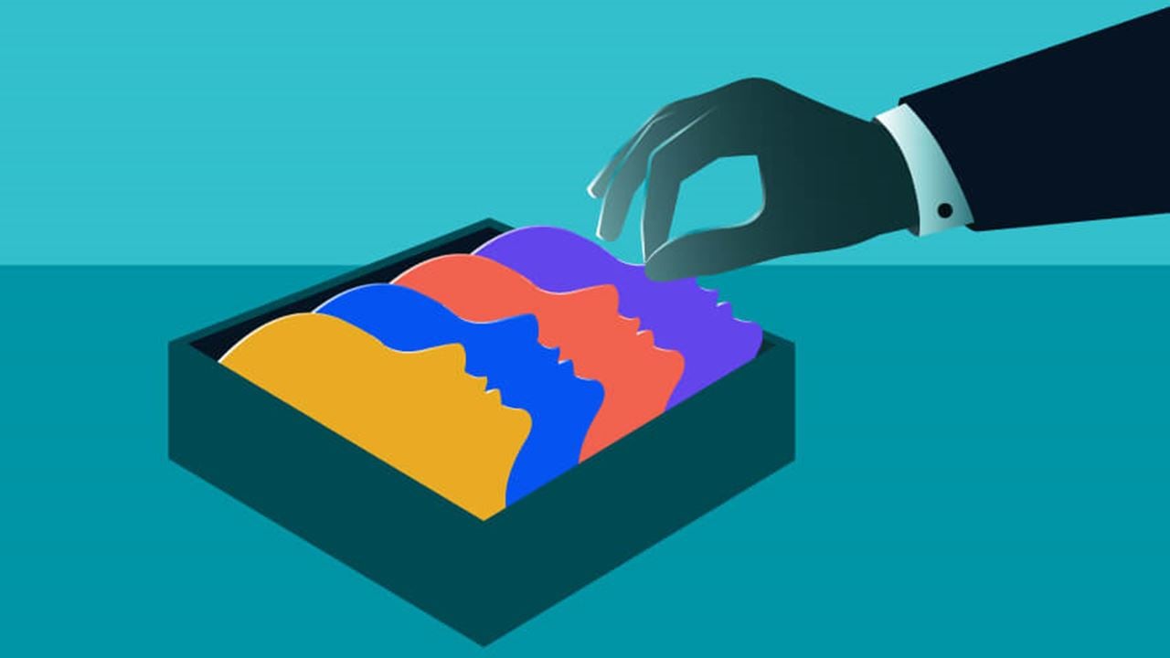 A suited hand reaches into a box of colorful overlapping face profiles, symbolizing diverse workplace dynamics or interpersonal conflict.