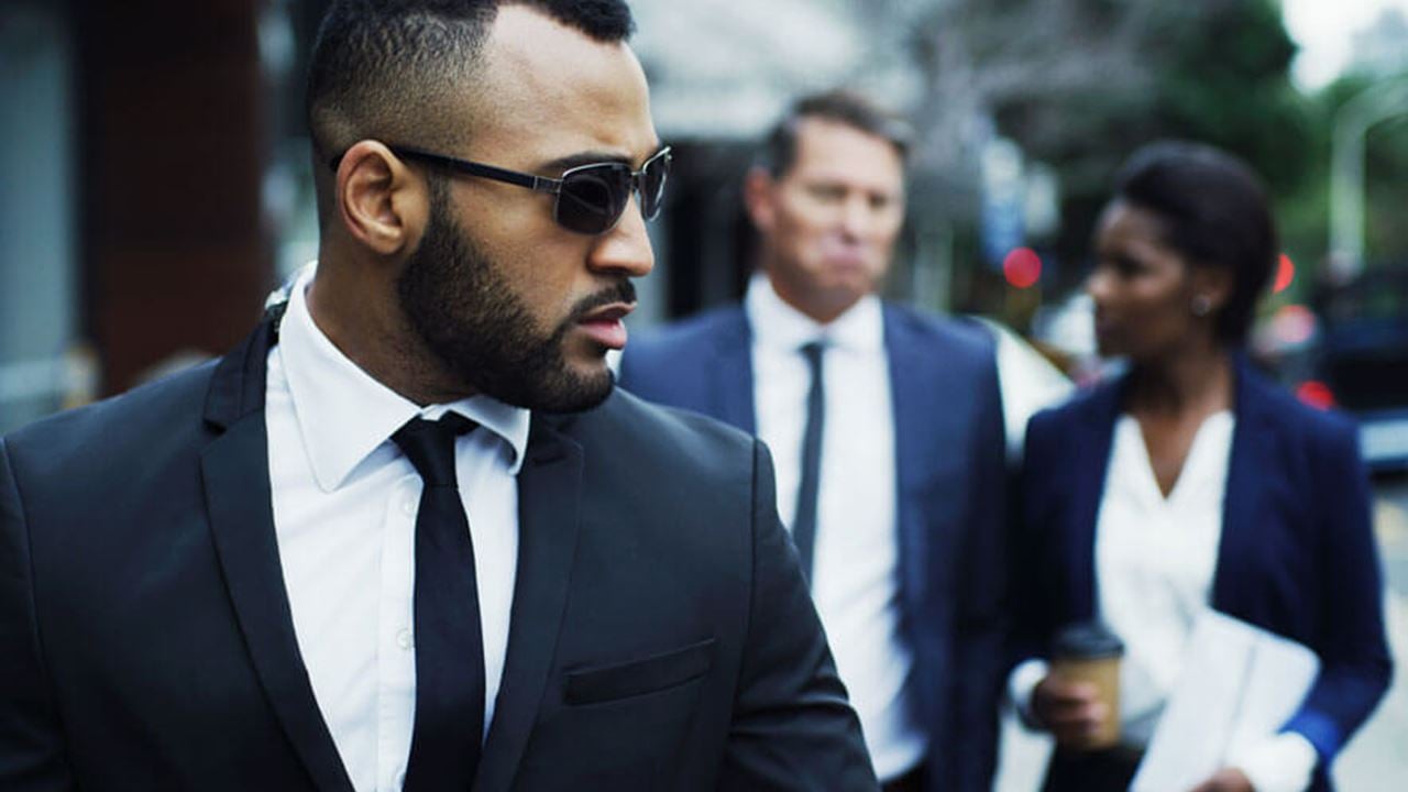 Photo of a male, suited close protection professional watching for threats to two executives following behind him