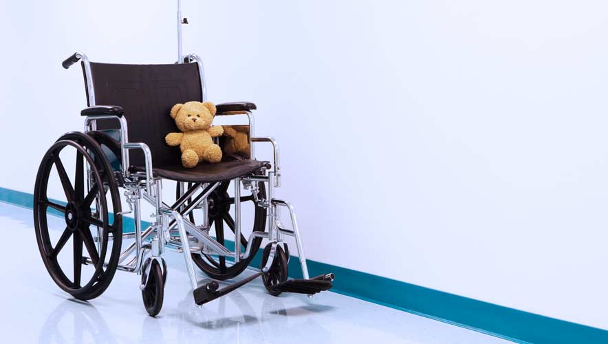 An wheelchair with a teddy bear seating in it sits in a hospital hallway. 