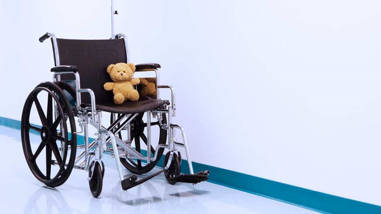 An wheelchair with a teddy bear seating in it sits in a hospital hallway.