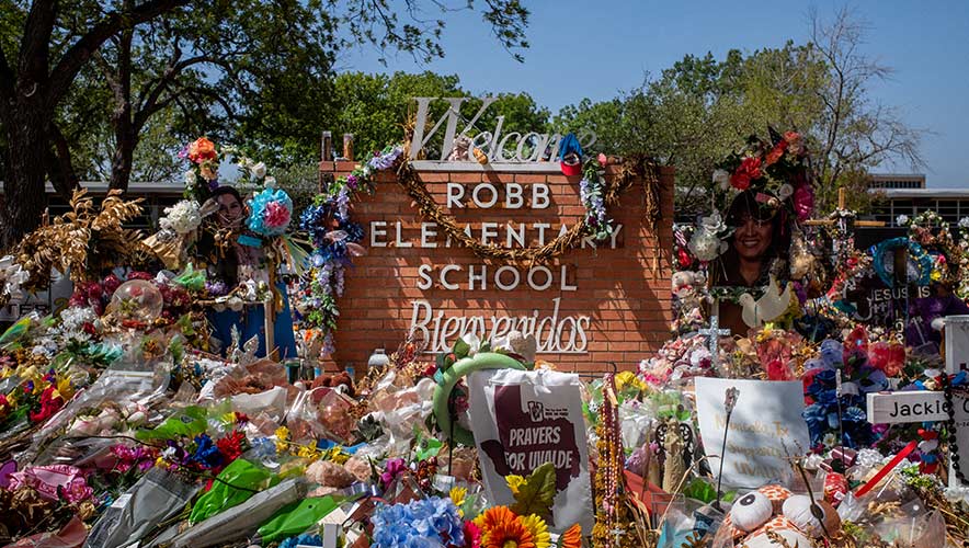 A memorial of flowers adorn a welcome sign at Robb Elementary School in Uvalde, Texas.  