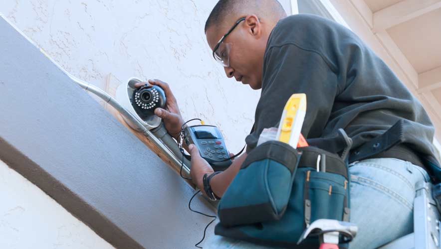 Man installs security camera on the side of a building. How can you enhance your organization’s security systems? 