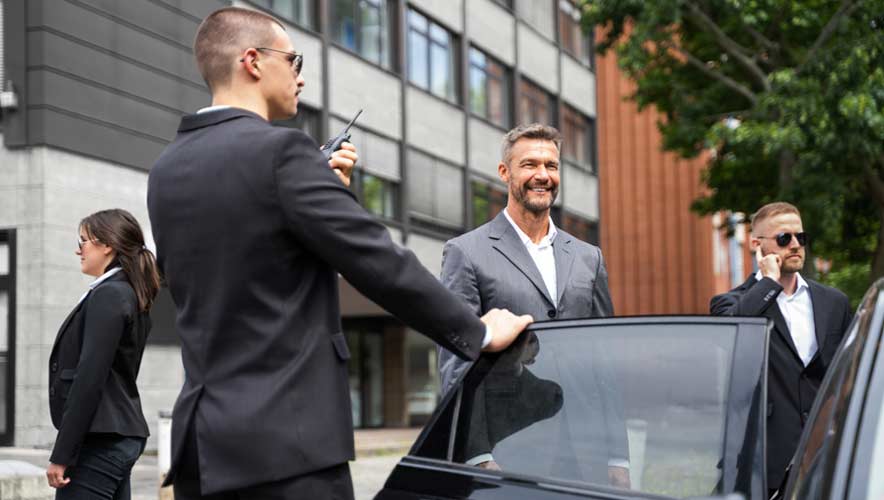 A group of three executive protection guards assists a high-profile person get into the back seat of a black car 